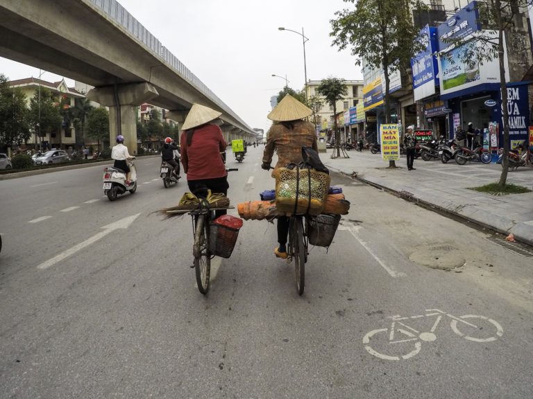 Two locals pedal across Hanoi in morning traffic.